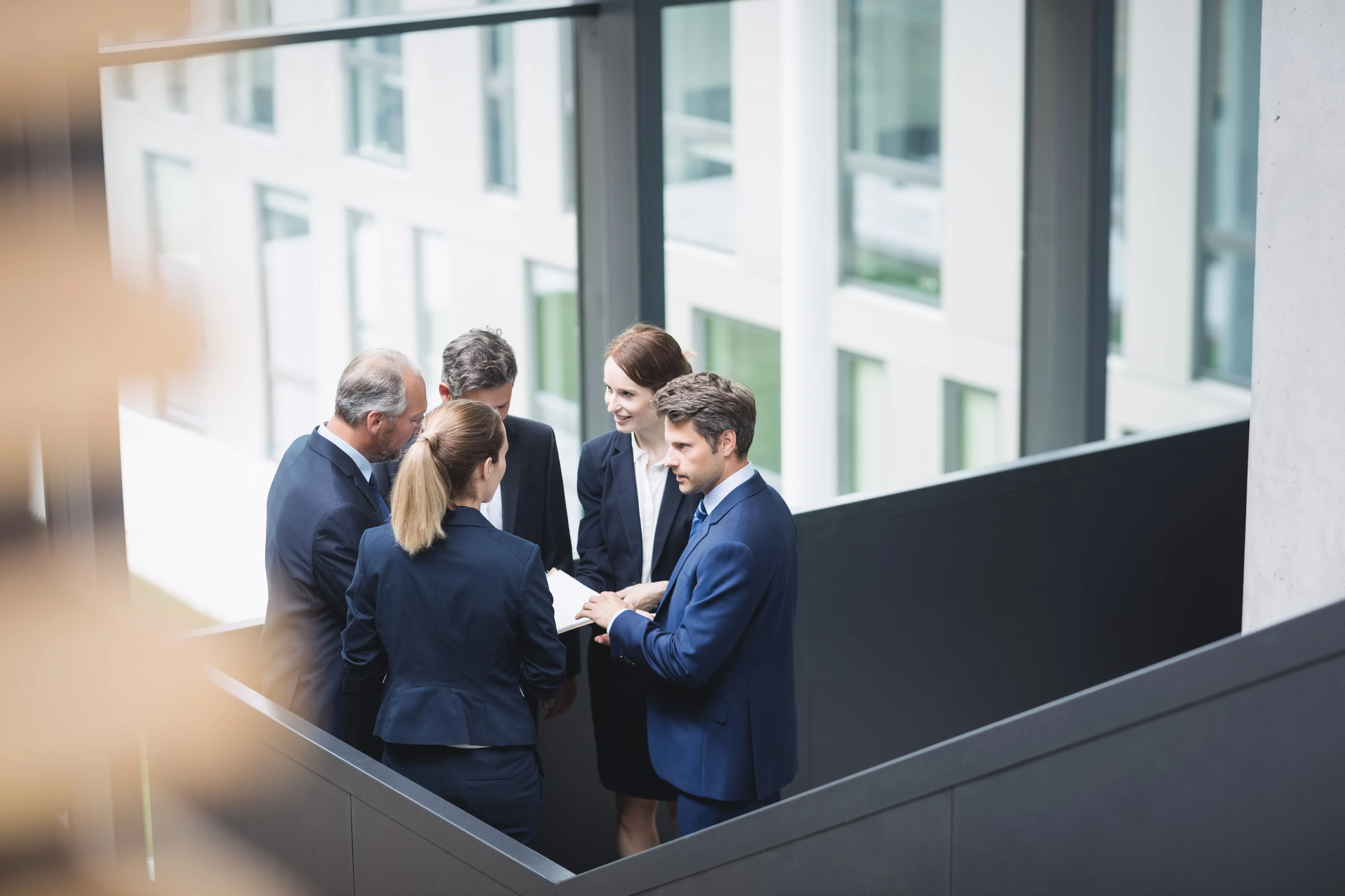 A group of business professionals in discussion inside a modern office building.