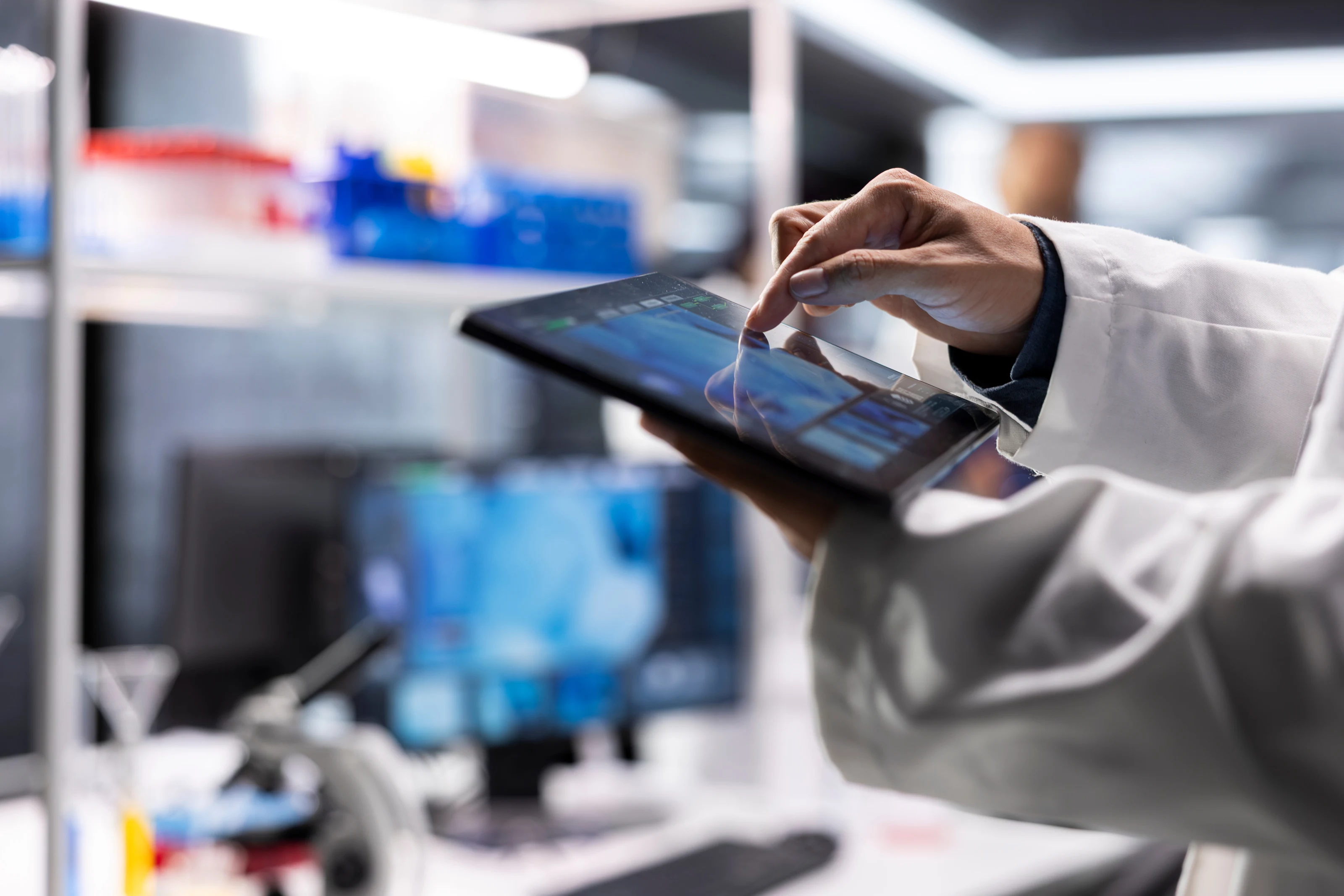 A researcher in a white coat reviewing data on a tablet inside a laboratory.
