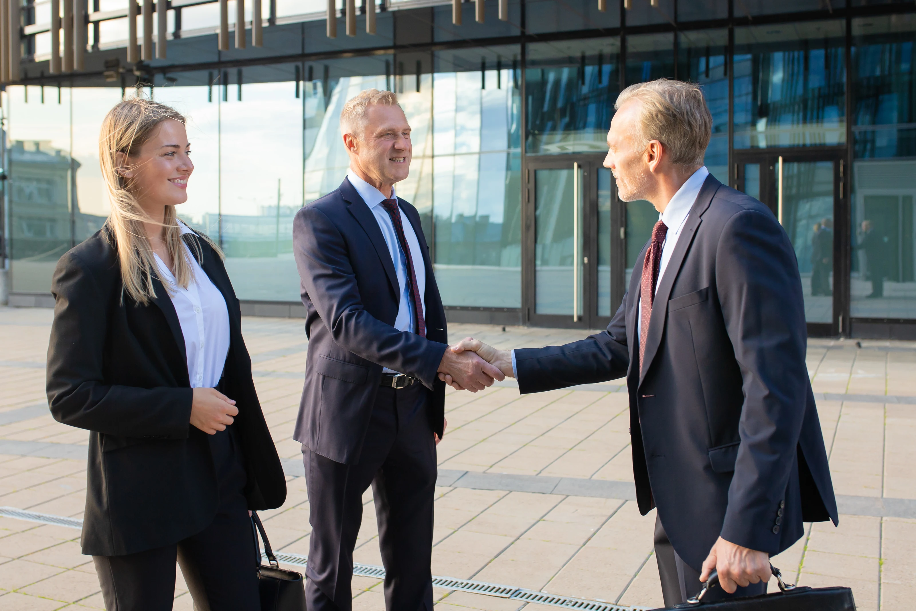 Business partners shaking hands outside a glass office building.