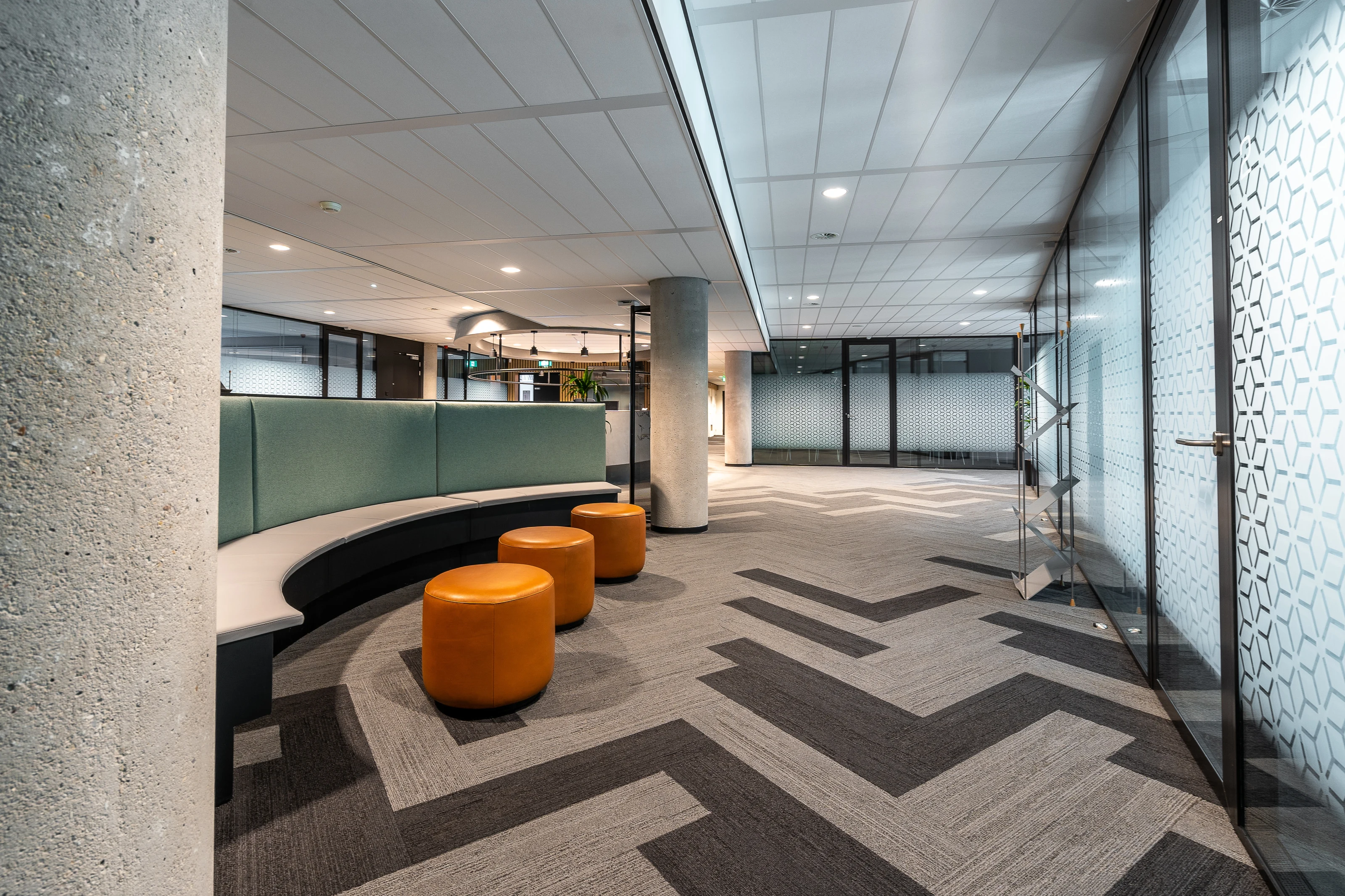 The interior of a modern open plan office with glass partitions and curved seating.