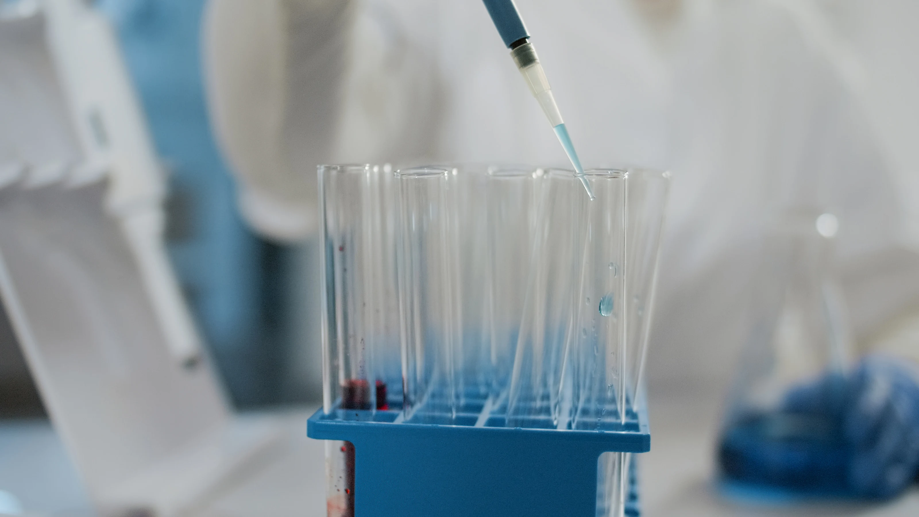 A micropipette dispensing into a rack of glass test tubes.