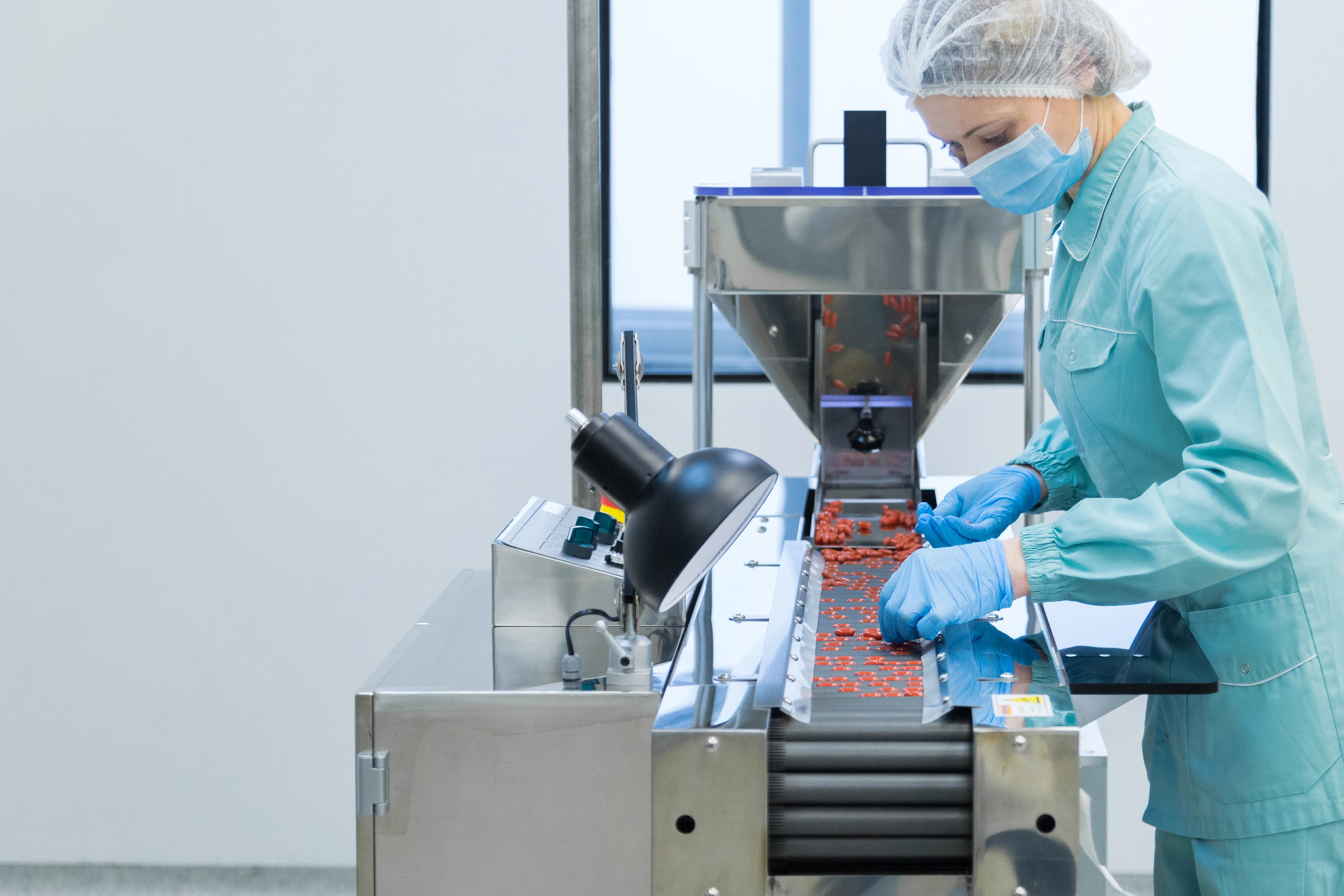 A worker in protective clothing operating a tablet-production machine on a pharmaceutical line.